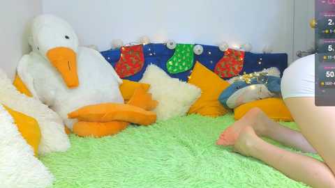 Video of a festive room with a large white duck plush, green plush carpet, blue cushions, orange socks, and Christmas decorations, including red and green stockings.