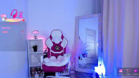 Video of a well-lit, cozy gaming room featuring a pink and white gaming chair, a white shelf with neon lights, and a large mirror reflecting a white door.