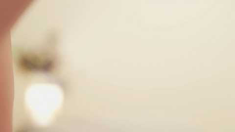 A blurred, close-up video of a person's lower body, possibly female, with a soft, pale background. The image lacks clear details, making identification difficult.