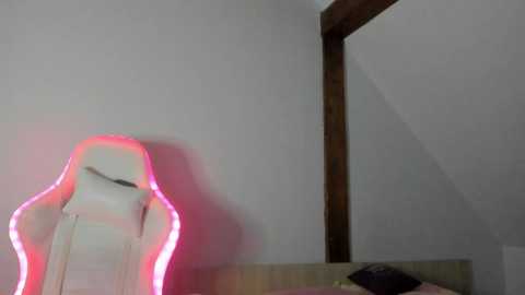 A video of a white gaming chair with a pink LED light, positioned against a plain white wall with a wooden frame, in a dimly lit room.