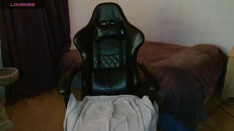A video of a black gaming chair with a gray cloth draped over its backrest, situated in a dimly lit room with brown furniture and a wall-mounted TV.