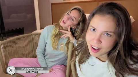 Video of two blonde women, one sitting on a wicker chair, the other standing, in a cozy indoor setting with wooden furniture.