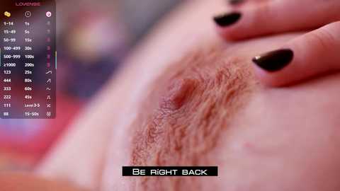 Media: Video of a close-up of a woman's vulva with black-painted nails resting on it, accompanied by a \"Be Right Back\" text. Background is blurred, with a digital interface on the left.