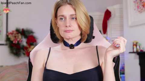 Video of a blonde woman in a black dress, adjusting a pink neck brace, in a festive, softly lit room with Christmas decor.