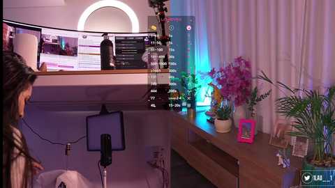 Video of a modern, dimly lit room with a wooden desk, a laptop screen displaying a calendar, potted plants, and a large round mirror.