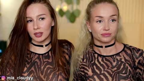 Media: Video of two young women with fair skin, long brown hair, wearing black choker necklaces and patterned long-sleeve tops, posing side by side.
