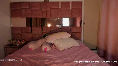Video of a pink-themed bedroom with a plush teddy bear and pillows on a bed, against a padded pink wall with a mirror.