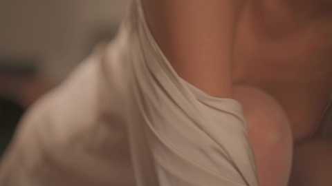 A blurred video captures a person with a light skin tone, wearing a white, off-the-shoulder top, with the focus on their shoulder and upper arm. The background is out of focus, suggesting an indoor setting.