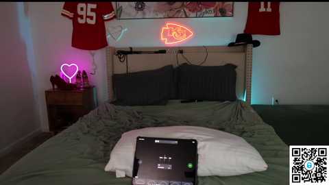 Video of a cozy bedroom with a bed, two red football jerseys, a neon heart, and a glowing fish.