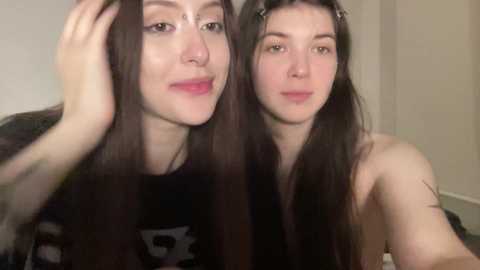 Video of two young women with long black hair, pale skin, and light makeup, one with a cow patterned shirt, smiling, indoors.