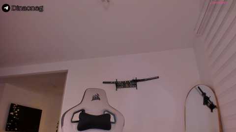 Video of a minimalist, white-walled room with a black gaming chair, a wall-mounted TV, and a large oval mirror reflecting the room.