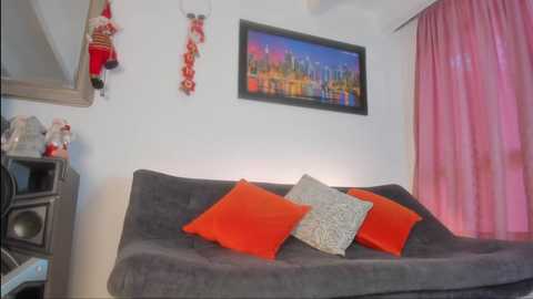 Video of a cozy, modern bedroom with a gray couch, red and gray pillows, Christmas decorations, and a vibrant cityscape painting.