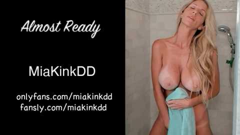 Video of a blonde woman with large breasts, wet hair, and a towel, standing in a shower. Text overlay advertises OnlyFans and Mikinkdd.
