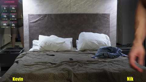 Video of a modern bedroom with a gray upholstered headboard, two white pillows, and a messy gray bedspread. A smartphone and a blue shirt are on the bed.