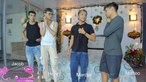 Video of four Asian men in casual attire, smiling, standing in a festive, decorated bedroom.