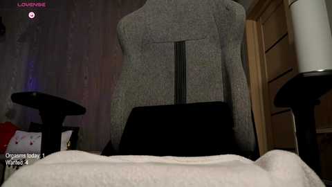 Video of a gray knit sweater mannequin in a dimly lit room, featuring a black chair, a white lamp, and a wooden door.
