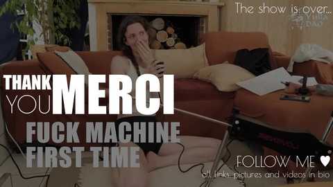 Media: A video featuring a woman in a brown tank top and shorts, seated on a brown couch with a fireplace behind her. Text overlays read \"Thank You MerCI Fuck Machine First Time\" and \"Follow Me.\