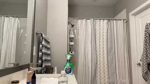 Media: A video of a modern, minimalist bathroom with a white shower curtain, gray walls, and a clean, white countertop. A green and white cleaning spray bottle and a black toothbrush are visible on the counter.