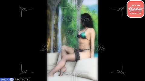 A video of a woman in black lingerie, sitting on a white couch, with a blurred background featuring a waterfall and greenery.