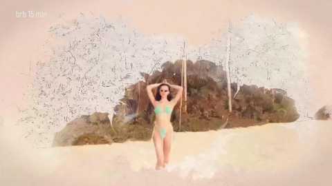 A woman with long brown hair stands in shallow water, wearing a green bikini, with a background of a sandy beach and trees. The image has a soft, dreamy filter.