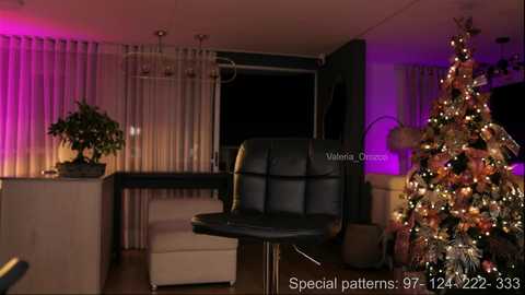 Video of a modern living room with a black leather chair, a decorated Christmas tree, and purple lighting.