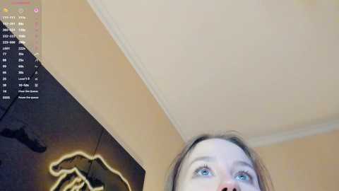 Media: Video of a young woman with fair skin and blue eyes, taken from below. She has light brown hair. The image is split into two halves: a computer screen showing a game and a close-up of her face.