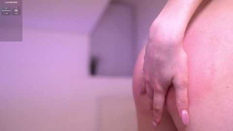 A video of a fair-skinned hand with neatly manicured nails resting on a pale, smooth surface. The background is a blurred, soft-focus indoor setting with muted, neutral tones.