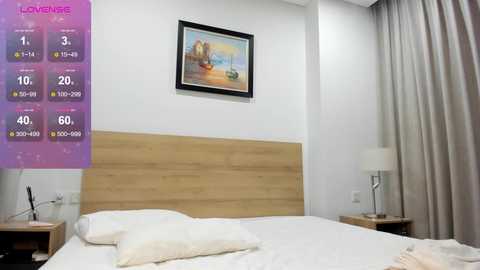 Video of a modern, minimalist hotel room with a wooden headboard, white bedding, a colorful landscape painting, and a digital temperature display on the wall.