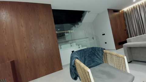 Video of a modern, minimalist living room with a wooden wall, beige sofa, and blue blanket on a wicker chair.