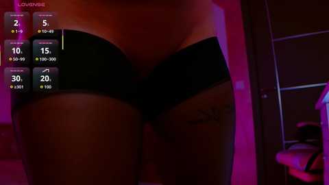 Video of a close-up of a woman's lower torso in black lingerie, with a tattoo on her left thigh, in a dimly lit room with purple and pink hues.