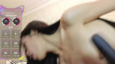 A blurry video of a naked woman with long black hair, lying on a bed, with a digital interface overlay showing health stats.