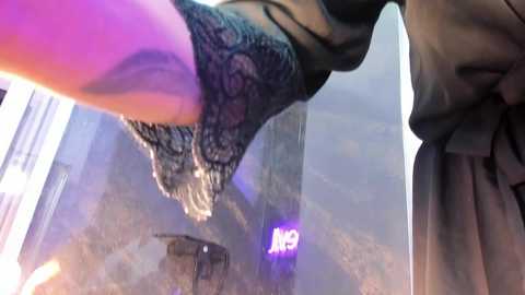 Video of a person wearing a black lace dress, standing on a balcony, with a view of a cityscape and a glowing \"AR\" sign in the background.