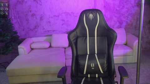 Video of a modern, black gaming chair with white accents, positioned in front of a cream-colored sectional sofa against a purple-lit, textured wall.