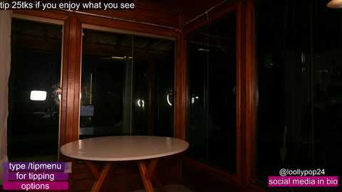 Video of a dimly-lit room featuring a round table with a white tablecloth, wooden-framed glass doors, and a text overlay promoting a social media account.