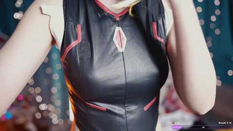 Video of a fair-skinned woman wearing a tight, black leather bodysuit with red accents and a V-shaped neckline. Background features blurred bokeh lights and a teal curtain.