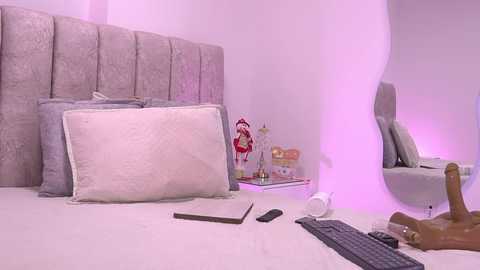 Video of a modern, minimalist bedroom with a plush gray headboard, white pillows, a smartphone, and a realistic sex doll on a bed.