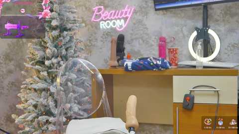 Video of a modern room with a white chair, snow-covered Christmas tree, neon \"Beauty Room\" sign, makeup mirror, and various beauty products.