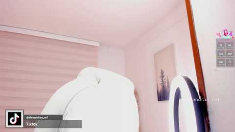 Video of a minimalist, white-walled room with a white leather chair, wooden wall paneling, and a round mirror on the right. A digital clock with pink numbers hangs on the wall.