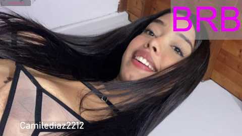 Video of a smiling, light-skinned Asian woman with long black hair, wearing a sheer black bra. Background features wooden flooring and a white wall. Text \"BRB\" in pink, \"camielucia22212\" watermark.