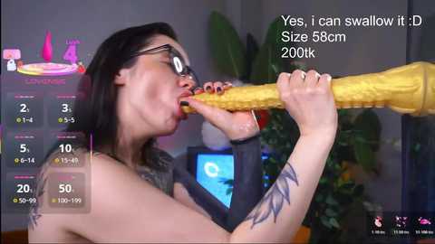 Video of a tattooed woman with glasses, topless, performing oral sex on a large, yellow dildo in a dimly lit room. A virtual reality game interface with stats is overlaid.