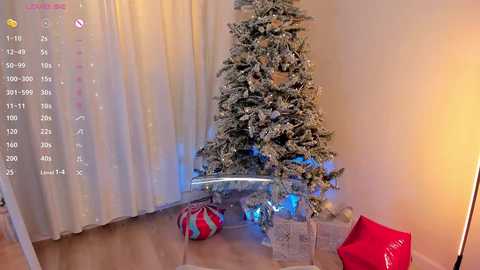 Video of a decorated Christmas tree with white snow-like coating, standing in a corner with a red and white striped gift under it, surrounded by white and red gift bags.