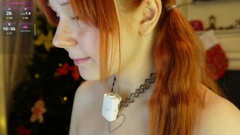 A video of a pale-skinned redhead with long, straight hair in a ponytail, wearing a black lace choker and a white iPod with a heart pendant, set against a blurred holiday-themed background with a Christmas tree and red ornaments.
