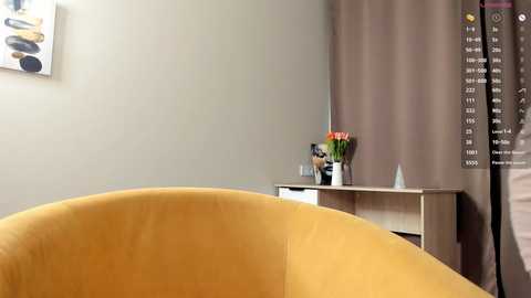 A video of a modern living room featuring a mustard-yellow curved armchair, a minimalist white console table with a vase of flowers, and beige curtains.