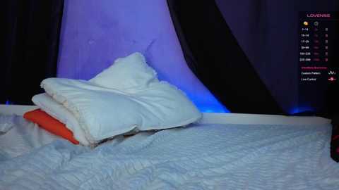 Video of a white pillow and orange blanket on a light blue quilted bedspread, set against dark curtains with a blue light. Twitch streaming platform overlay in the top right corner.
