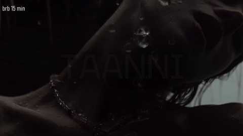 A close-up video of a person's wet, dark-haired head, with a thin chain necklace, taken in dim lighting. Water droplets are visible on the skin.