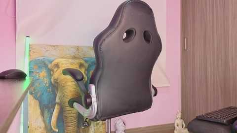 Video of a black gaming chair with ergonomic design, sitting in a room with a wall mural of an elephant and a wooden door.