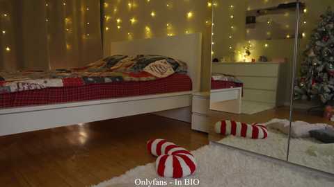Video of a cozy bedroom with a white bed, red and white striped socks, a festive tree, and soft yellow fairy lights on the wall, creating a warm, holiday ambiance.