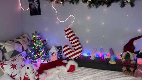 A festive bedroom scene with a decorated Christmas tree, red and white striped stockings, twinkling fairy lights, and plush toys, creating a cozy, holiday ambiance.