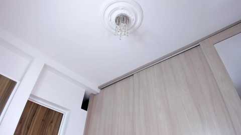 Video of a modern, well-lit room featuring a white ceiling with a chandelier, light-colored wooden sliding doors, and white walls. The setting suggests a contemporary interior design.