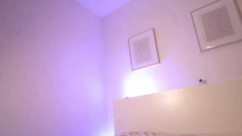 A minimalist, modern video of a white-walled corner room with two framed minimalist line drawings on the upper wall, and a soft, purple LED strip light casting a gentle glow on the lower wall.